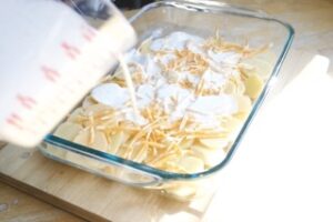 Layerd potatoes, cheese and creamy mix into a dish prepped for cheesy potato bake