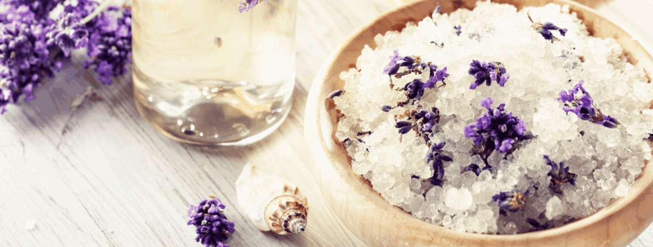 bowl of lavender bath soak with a glass of lavender essential oil