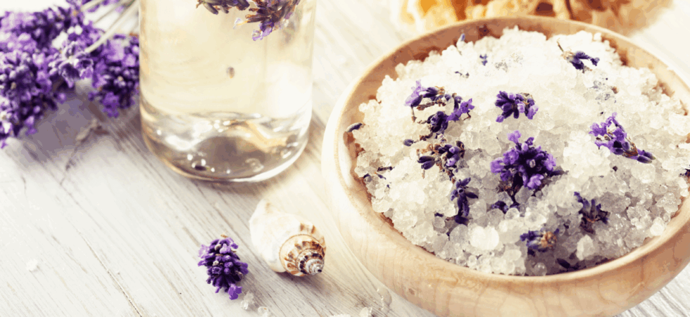 bowl of lavender bath soak with a glass of lavender essential oil