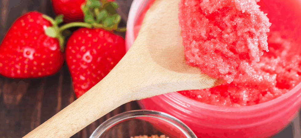 Strawberry sugar scrub on a spoon next to brown sugar and strawberries